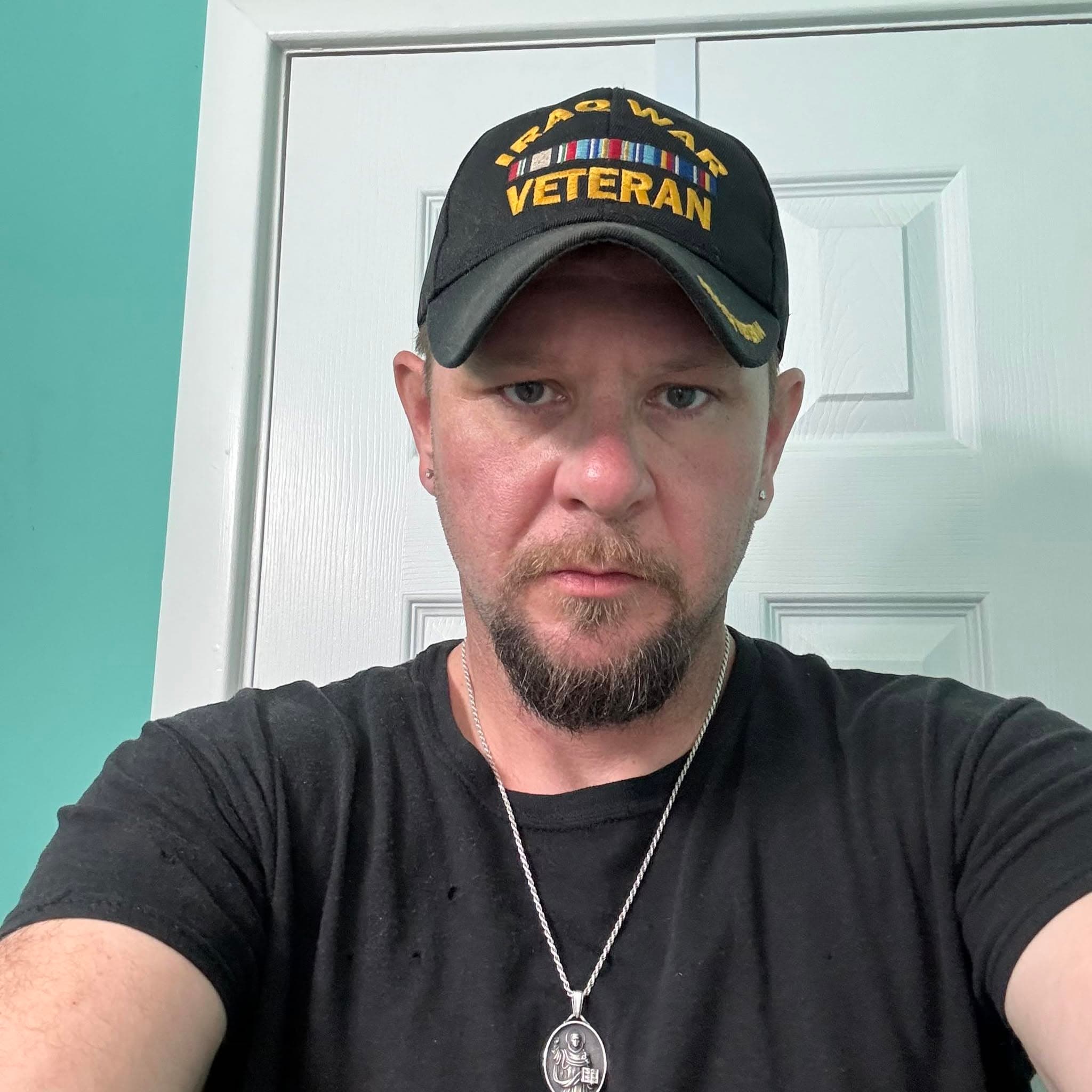 Portrait of Bill Lyman wearing a black cap embroidered 'Iraq War Veteran'