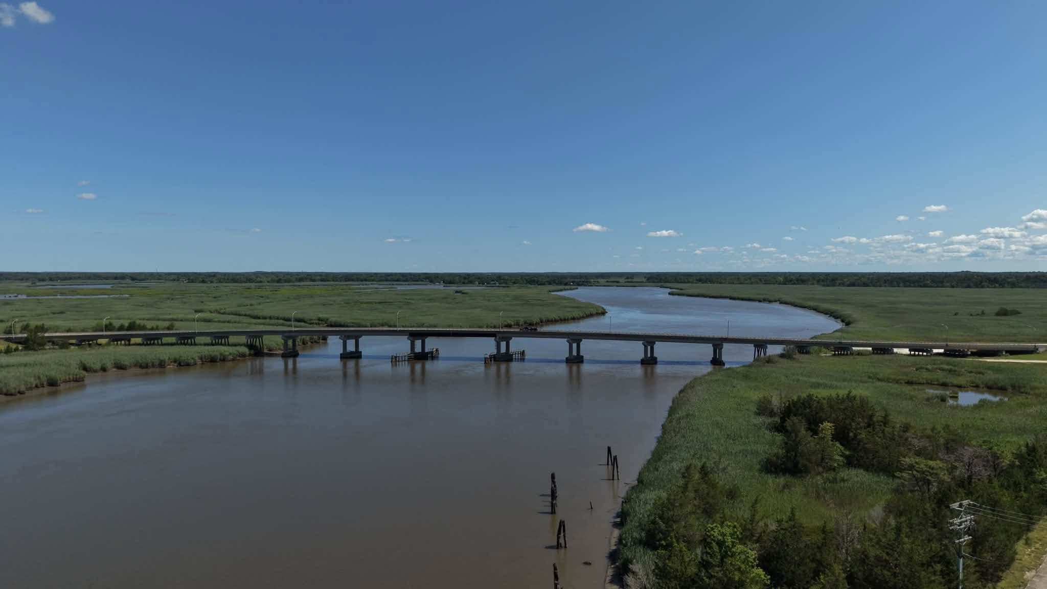 Aerial view of a two-lane bridge crossing a marsh river under a clear blue sky