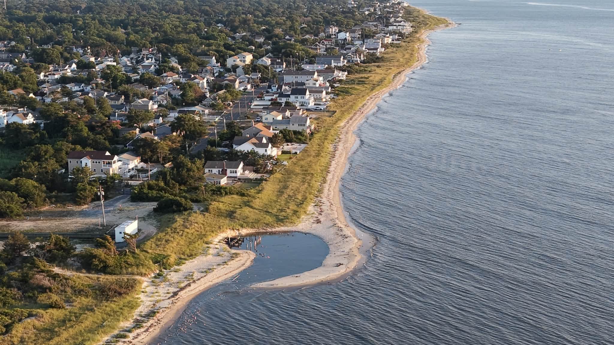Aerial view of a South Jersey barrier-island shoreline at golden hour, homes along the dunes with open bay water beyond