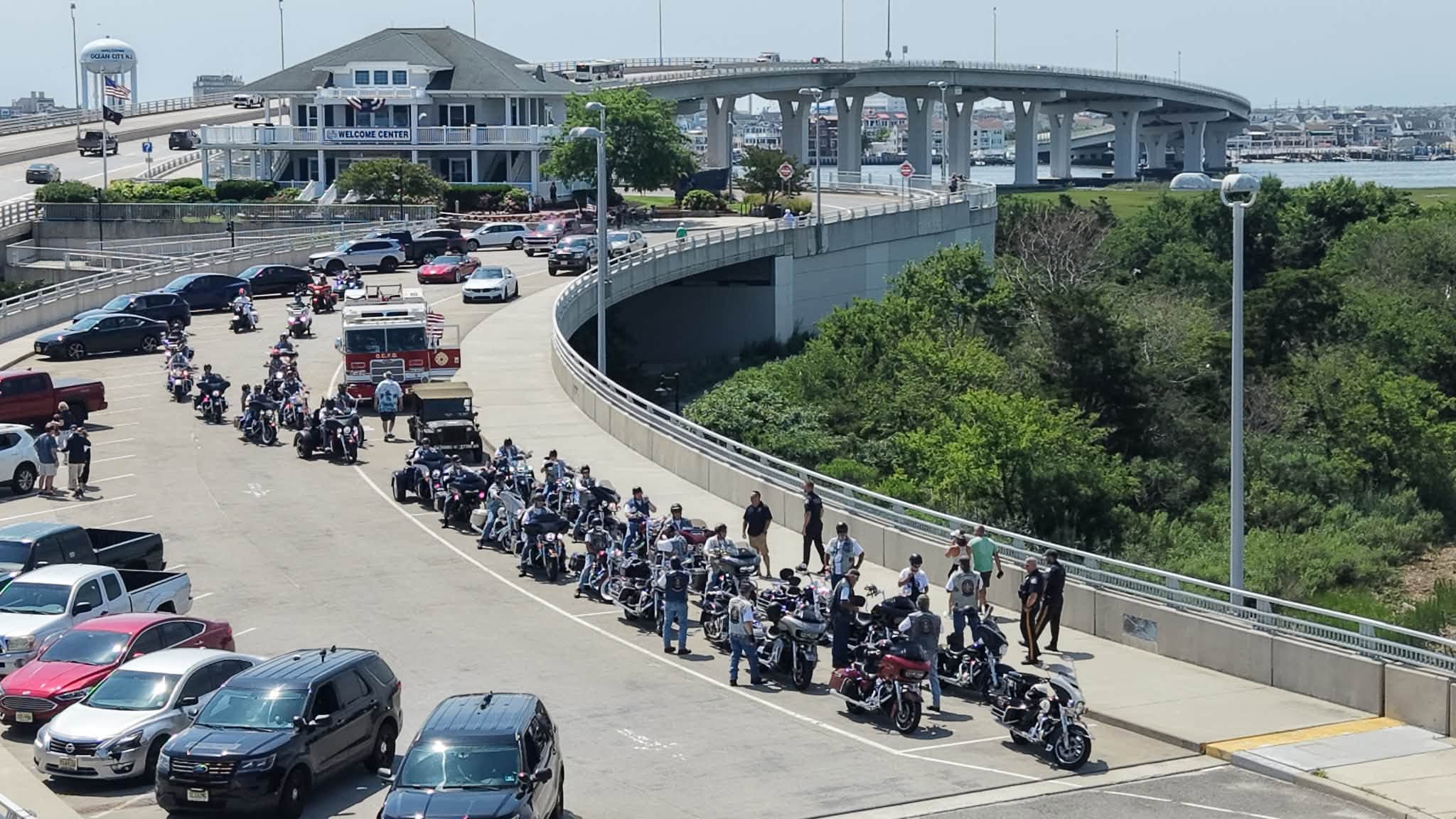 Aerial view of a motorcycle procession with police escort crossing a South Jersey shore-town bridge